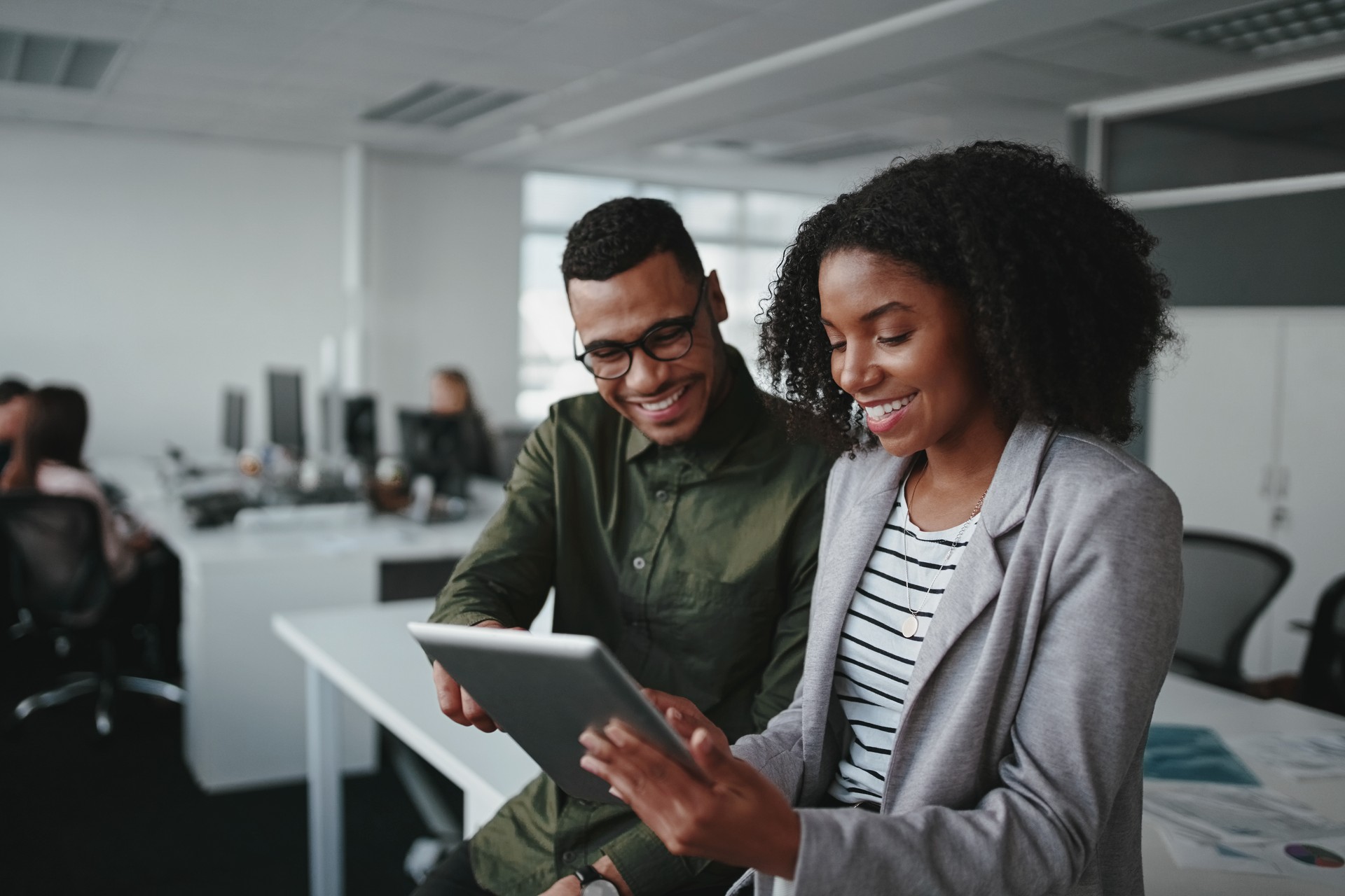 Smiling young african american professional businessman and businesswoman together working online with a digital tablet in office